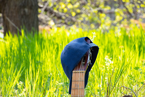 baseball blue cap hanging on an old guitar stands on a background of grass