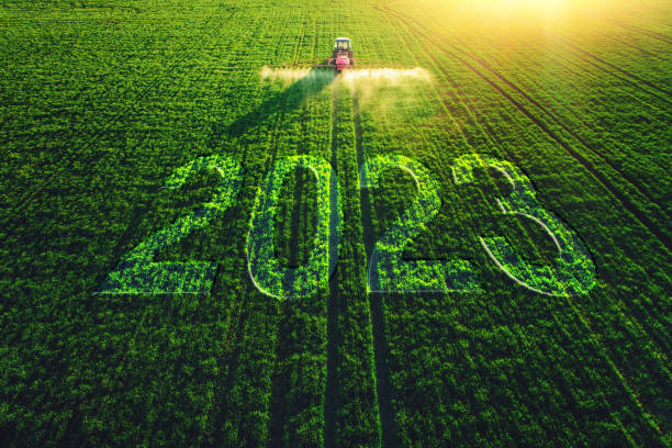2023 Happy New Year agricultural business concept. Aerial view of farming tractor plowing and spraying on green field stock photo