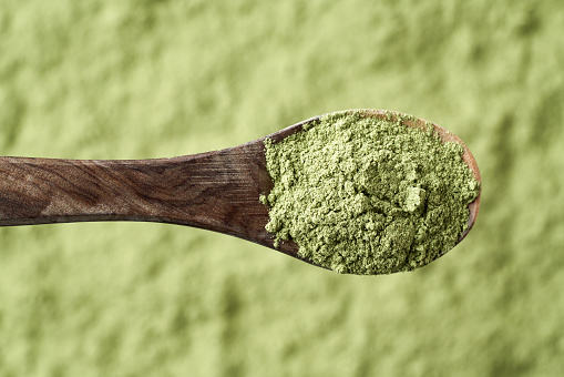 Barley grass powder on a spoon over green background, top view. Healthy nutritional supplement.