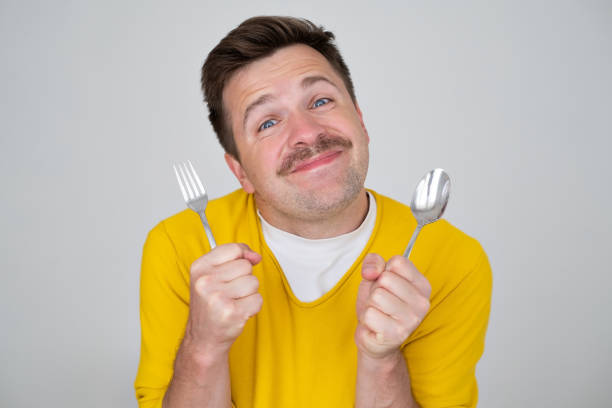 istock handsome hungry young man holding fork and spoon waiting for dinner 1446738486