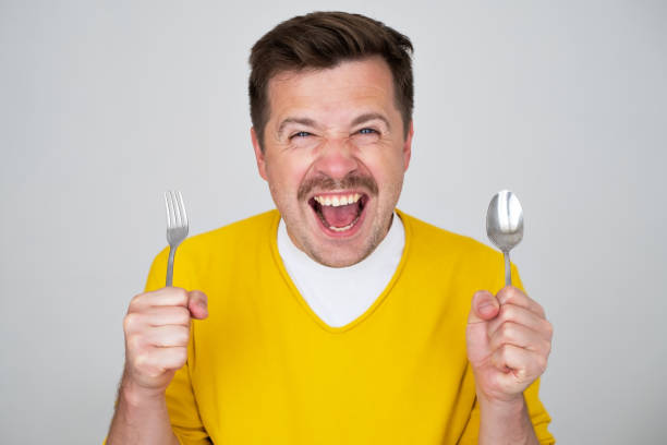 istock handsome hungry young man holding fork and spoon waiting for dinner 1446739183