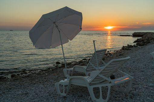 Empty deck chair and parasol on the beach at the sun set.