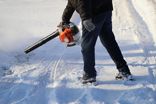 Worker cleaning pavement from snow with blower .