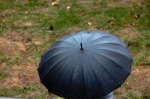 High angle view of an unrecognizable person walking in the rain under a dark blue umbrella