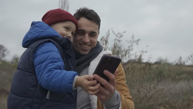 Positive father and son talking by video call on mobile on slope