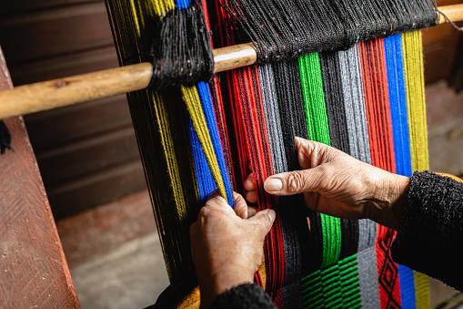 Unrecognizable latin elder woman's hands using a homemade craft loom to weave colorful wool