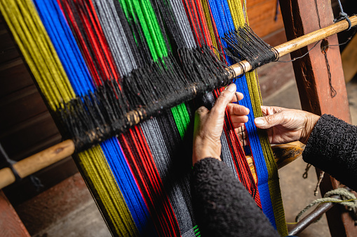 Unrecognizable elder woman's hands using a homemade craft loom to weave colorful wool