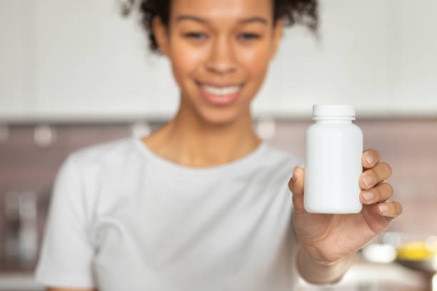 Healthy lifestyle concept. Happy young African American woman holding bottle of dietary supplements or vitamins in her hands stock photo