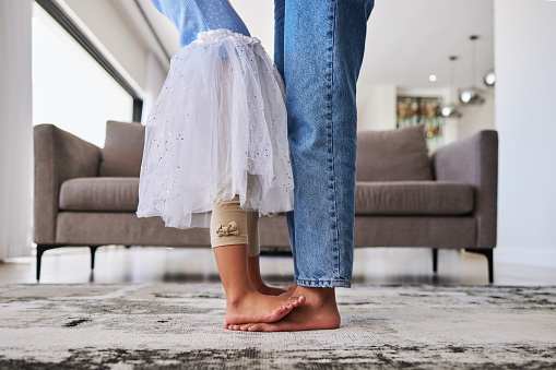 Feet, child and mother teaching a dance ballet movement on the living room floor together in their house. Legs of a girl kid learning and dancing to music with her mom in the lounge of their home