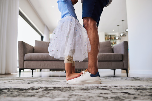 Feet, dance and girl and father dancing in a living room, love, family and fun in their home together. Shoes, happy family and parent teaching child dancer, loving, caring and support by single dad
