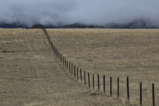 Landscape of fence dividing and continuing beyond view raises evocative questions about division, separation, equity, customs, and purposes.