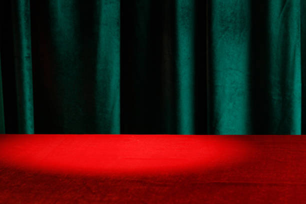 istock Modern background with empty red cloth table and green draped velvet curtains. Template for advertising, presentation. Light spot 1446755199