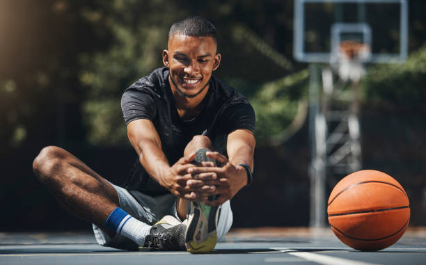Training, basketball player and man stretching legs in outdoor community court, muscle energy and healthy sports game performance. Happy, strong and young male athlete warm up exercise in competition entrenamiento, jugador de baloncesto y hombre estirando las piernas en la cancha comunitaria al aire libre, energía muscular y rendimiento saludable en el juego deportivo. atleta masculino feliz, fuerte y joven calienta el ejercicio en competición