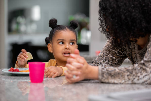 Adorable little girl sits at kitchen counter for dinner with her mother stock photo