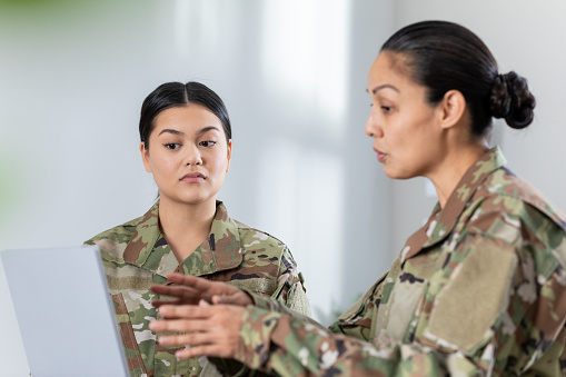 Female soldier meeting in office with commanding officer. Women are wearing camo clothing