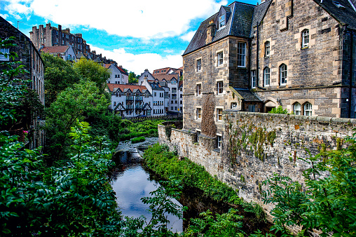 A picturesque scene where the Water of Leith winds around through Edinburgh Scotland and historic architecture can be seen on both sides of the river.