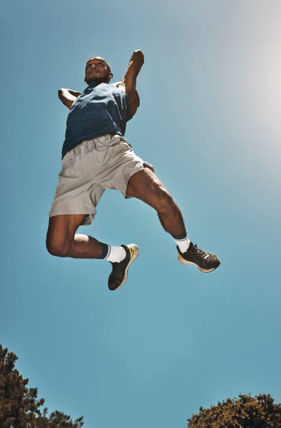 sports, blue sky and basketball man jump for game, competition or slam dunk training, practice or workout. high energy, athlete motivation and basketball player doing fitness or exercise bottom view - exercising motivation looking up african descent imagens e fotografias de stock