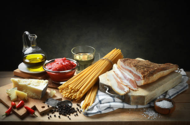 Ingredients for Amatriciana pasta. Bucatini, pancetta, peeled tomatoes, pecorino cheese, extra virgin olive oil, white wine, chilli and salt. Space for text. Spaghetti Amatriciana, famous Italian recipe, basic ingredients on wooden table, still life in rustic setting, gray background, copy space. all'amatriciana stock pictures, royalty-free photos & images