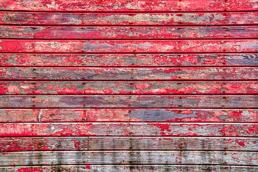 Old red horizontal weathered wood siding background with peeling paint