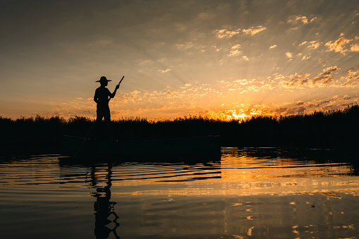 Fisherman in front of an early morning sunrise sky fishing out of his boat during a summer sunrise on lake