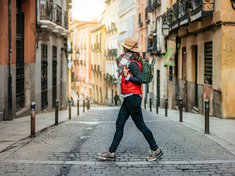 A tourist woman with cap and backpack, crosses a street in the historic center of Madrid. Walking tourism in spain. Concept of tourism and Spanish culture.