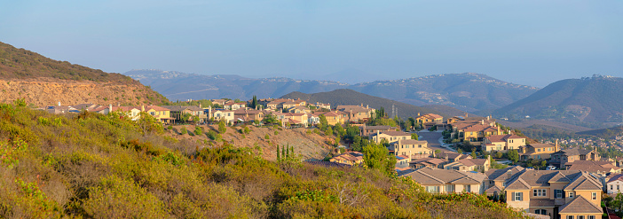 Suburban neighborhood on top of the mountains in Double Peak Park at San Marcos, California. There are large houses on a mountain on the left against the mountains at the back with residences on top.