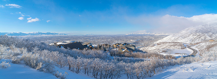 High angle view of Draper residential area in Utah. There are snow covered shrubs on the mountain and a plowed curved road on the right and houses on the left and at the bottom of the mountain.