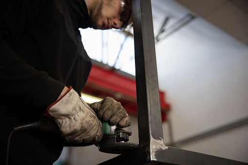 A worker uses a sander on a metal bar in a workshop