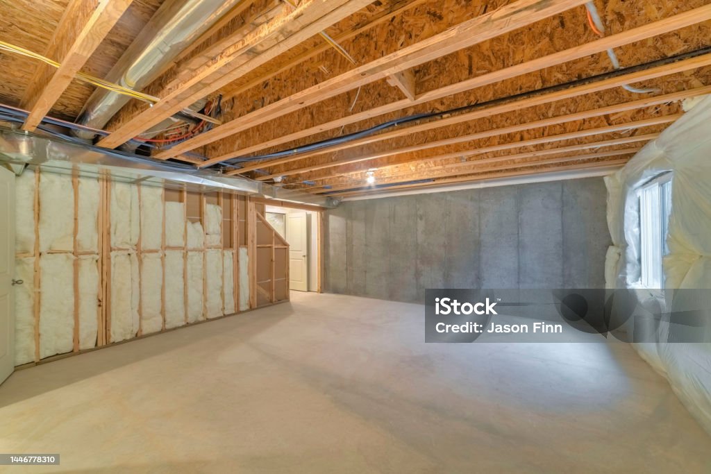 Unfinished basement with a plastic vapor barrier on the wall Unfinished basement with a plastic vapor barrier on the wall. Empty basement interior with wooden frameworks and insulated wall on the left and a window on the right. Basement Stock Photo
