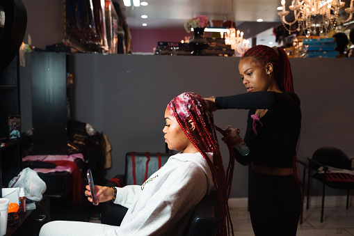 Hair stylist braiding a clients hair in a beauty salon.