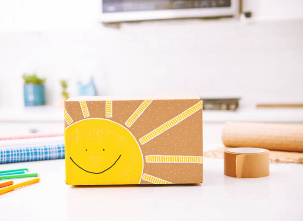 Handmade gift box with cute sunshine design on a kitchen island with gift wrapping supplies. Concept of shipping happiness. Artwork on gift boxes, designed and painted by photographer.