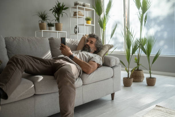 Mature man relaxes on the couch, browsing the net. stock photo