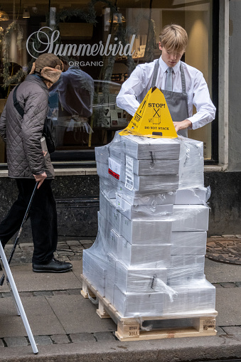 Copenhagen, Denmark, Nov 2, 2022 A young shop attendant attends to a palet of boxes and a sign sign saying Do Not Stack.