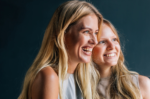 The love between a mother and daughter is forever: a charming Caucasian mother and her daughter smiling while they are looking away. (studio shot)