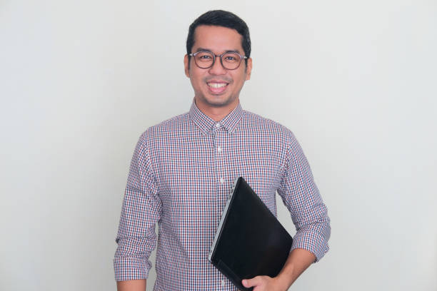 istock Adult Asian man smiling confident at camera while holding a laptop computer 1446790695