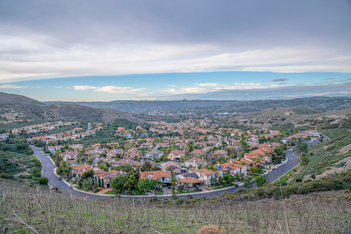 View of a subdivision from a mountain trail at San Clemente, California. There is a grassland at the front near the rich neighborhood below against the cloudy sky background.