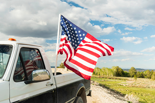 The American flag waving in the breeze on an old Ford truck, reflected in the window