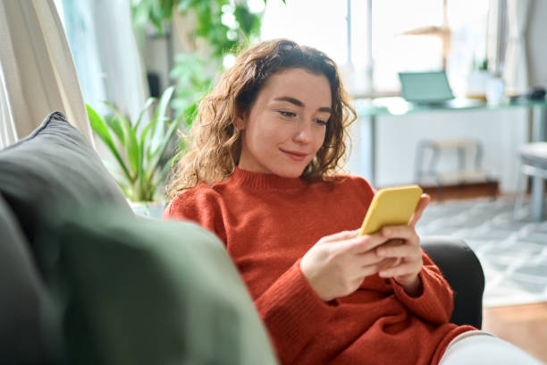 istock Smiling relaxed young woman sitting on couch using mobile phone technology. 1446806030