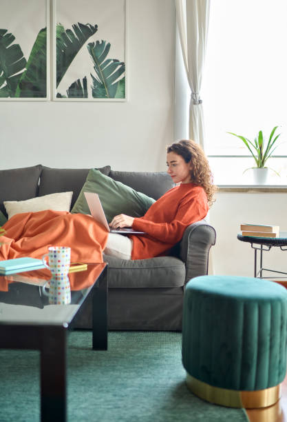 istock Relaxed young woman sitting on sofa using laptop at home cozy interior. 1446806039