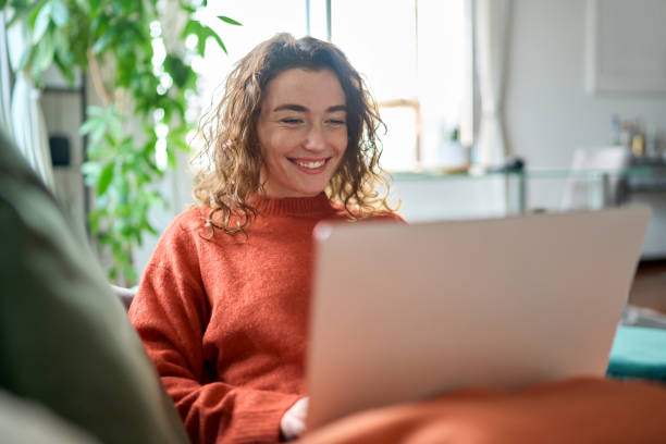 istock Relaxed happy young woman sitting on sofa using laptop at home surfing. 1446806041