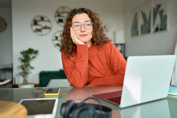 istock Young woman looking away and thinking while working on laptop computer at home. 1446806047