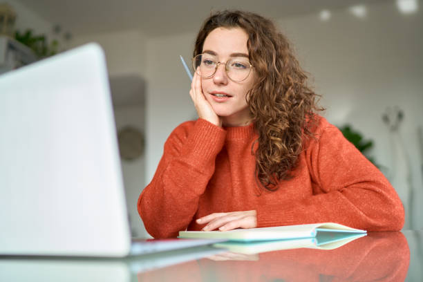 Young woman student using laptop watching online webinar writing at home.