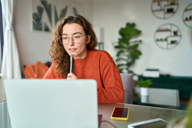 Young girl student looking at laptop watching online webinar learning at home.