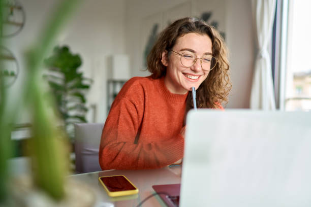 joven estudiante feliz usando computadora portátil viendo webinar escribiendo en casa. - aprender fotografías e imágenes de stock