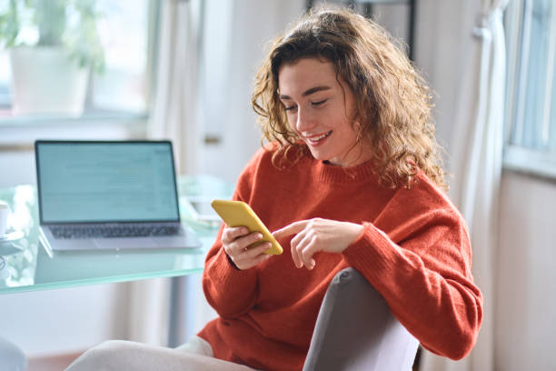 istock Smiling young woman holding cell phone using smartphone at home. 1446806083