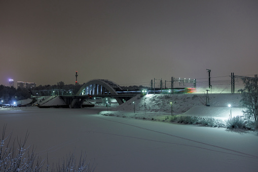 At night, a bridge crosses a frozen river in a winter park in Khimki, Moscow region, Russia.