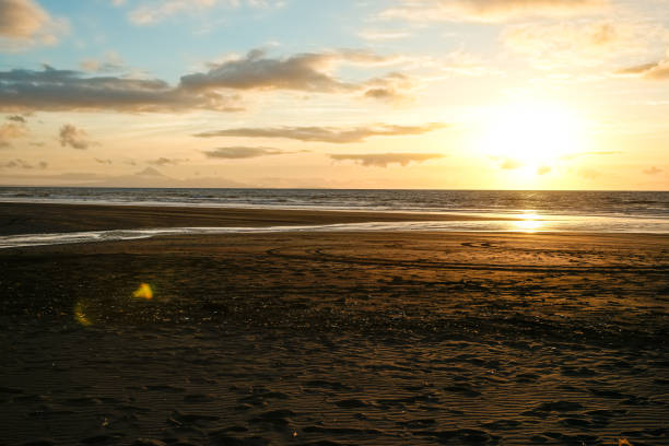 istock Beach in silhouette as sunsets on distant horizon over ocean. 1446809013