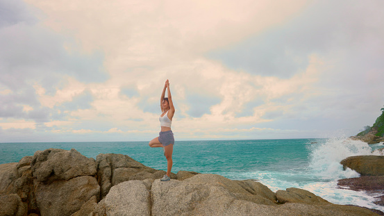 Asian woman improves balance for body, mind and spirit with yoga practice at beach on the rock on summer. Female Slow movements and deep breathing improves strength and flexibility. mental health
