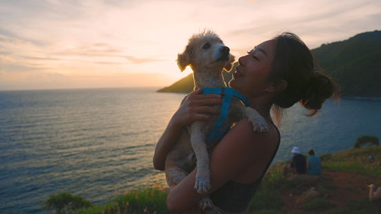 Candid Asian woman hugging dog happy on the beach at travel and vacation. Female Happy smile with pet as new life at sunset. life balance concept
