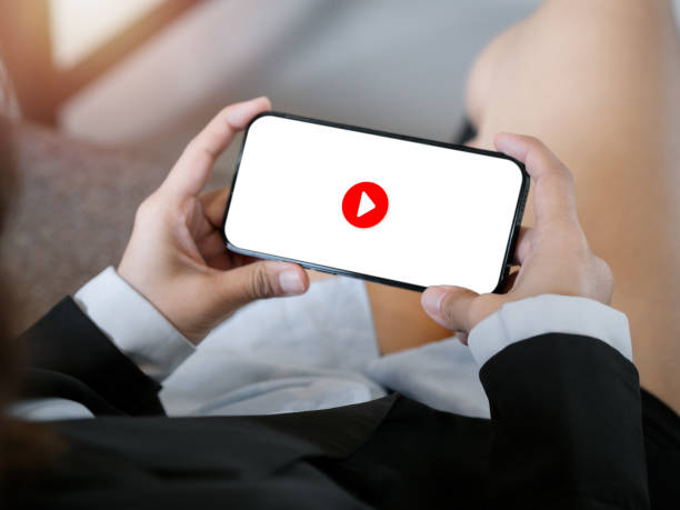 istock Red play button icon on white screen background on mobile smart phone, horizontal style holding by business woman's hands. Watching movie, entertainment or social network content, relaxing time. 1446812819